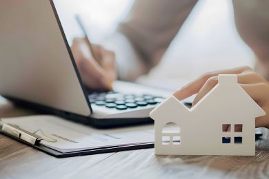 Foto: Person bearbeitet Akten, Modell eines Hauses im Vordergrund